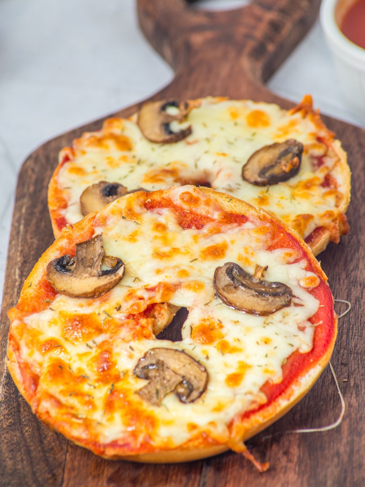Bagel pizzas topped with mushrooms on a wood board.
