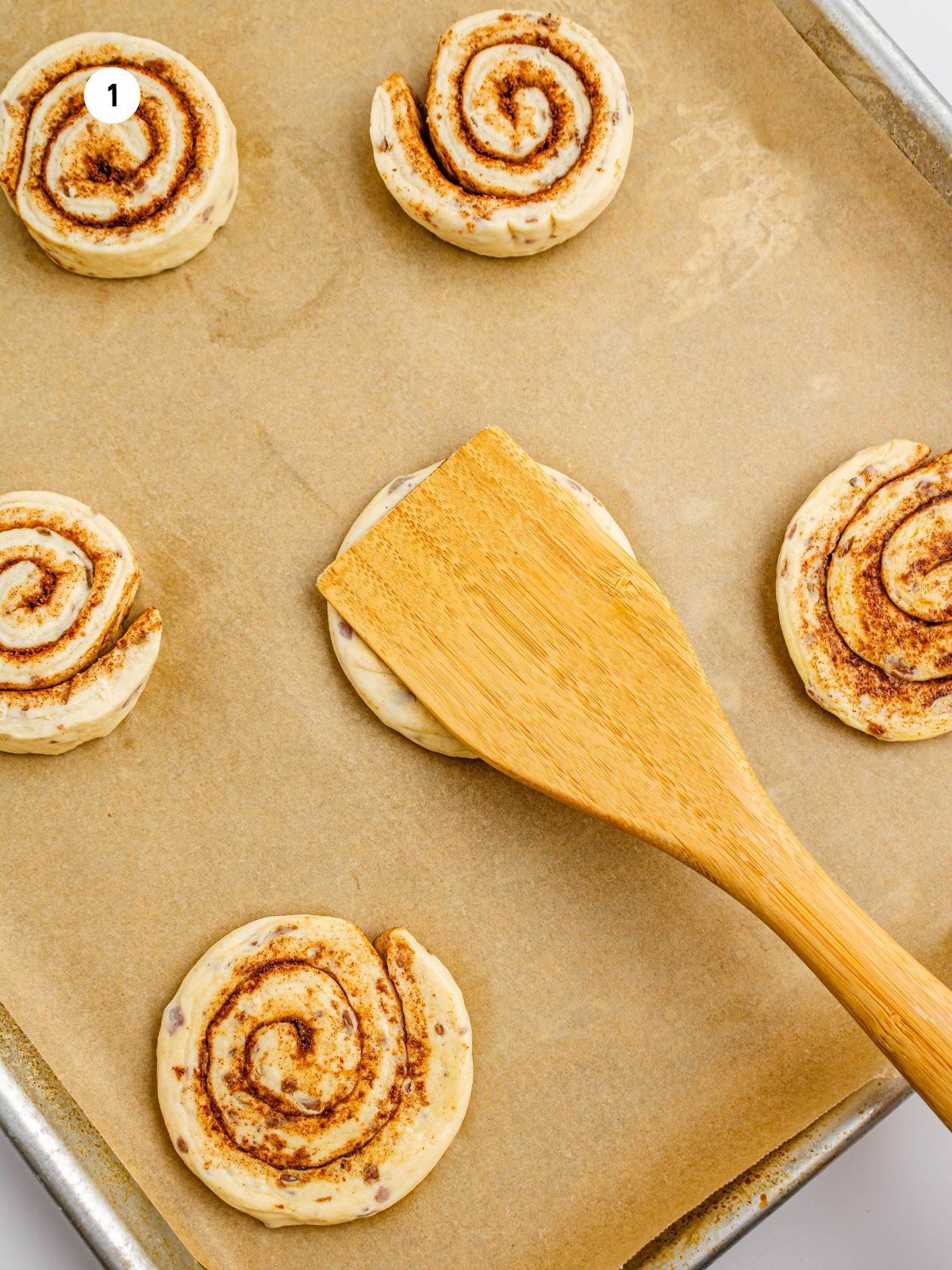wooden spatula flattening a refrigerated cinnamon roll.