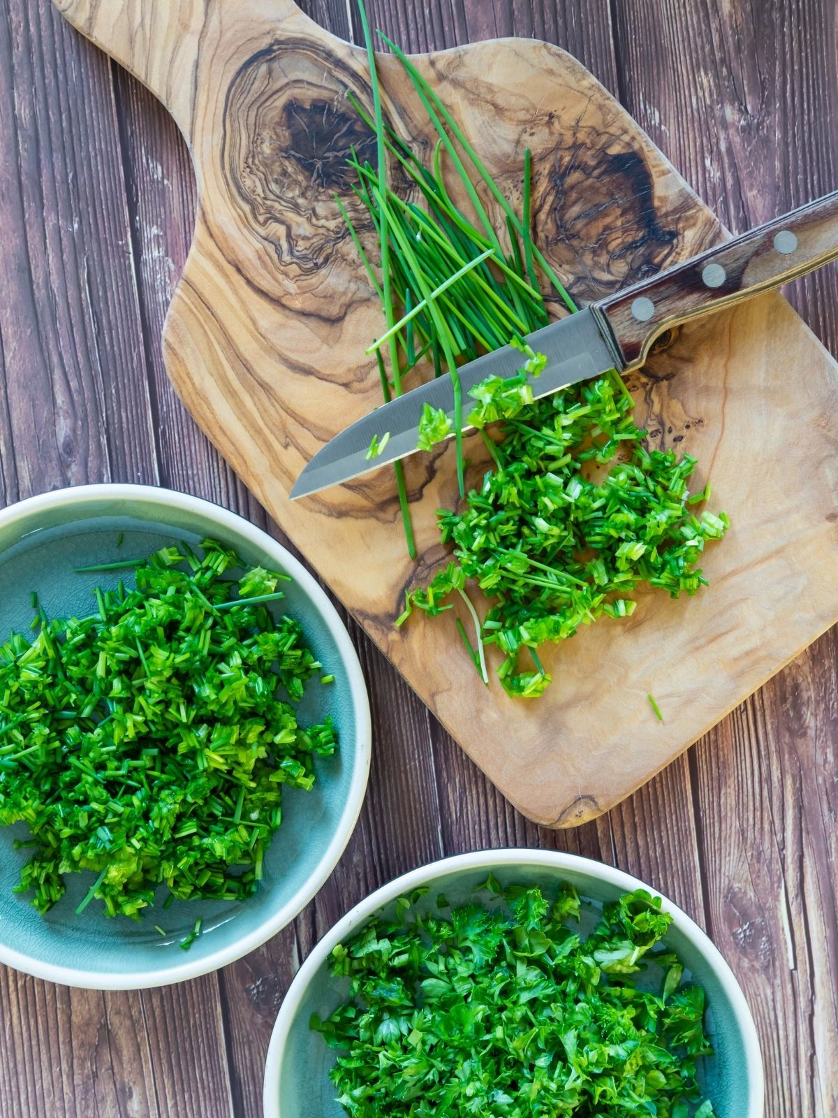 blue bowls with chopped herbs and on cutting board with knife.