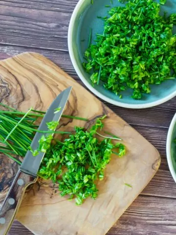 herbs in bowls and on cutting board with knife.
