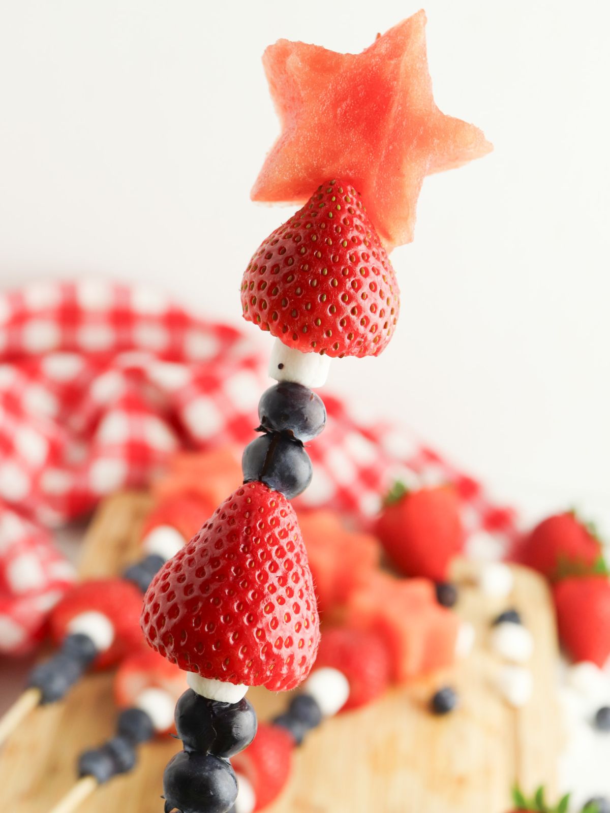 A fruit kabob held up to show it complete with more in the background.