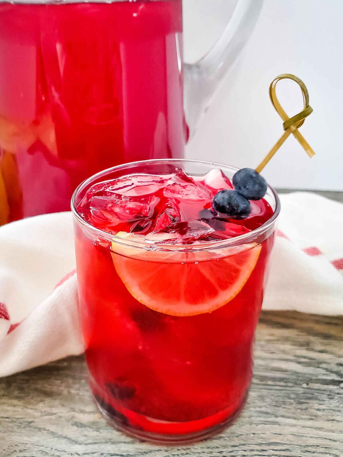 Blueberry Lemonade served in a glass with a wedge of lemon and a skewer of blueberries.