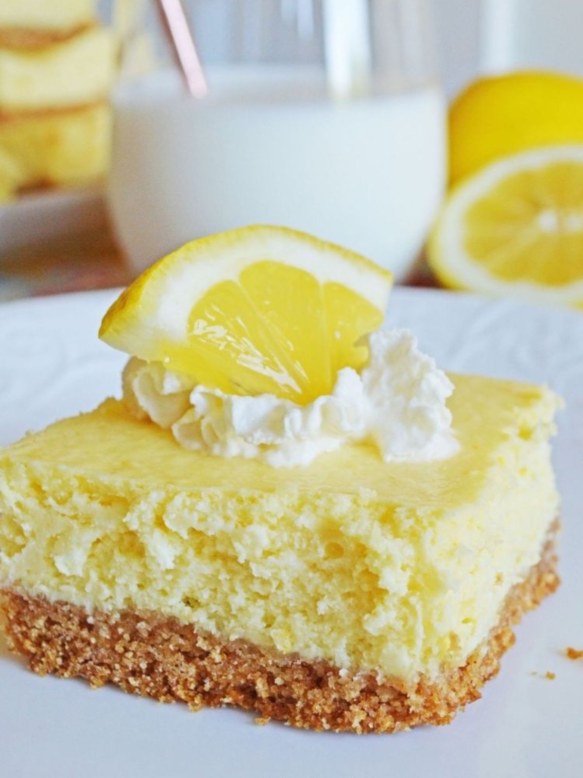 close up of lemon cheesecake bar served with a dollop of whipped cream and lemon wedge