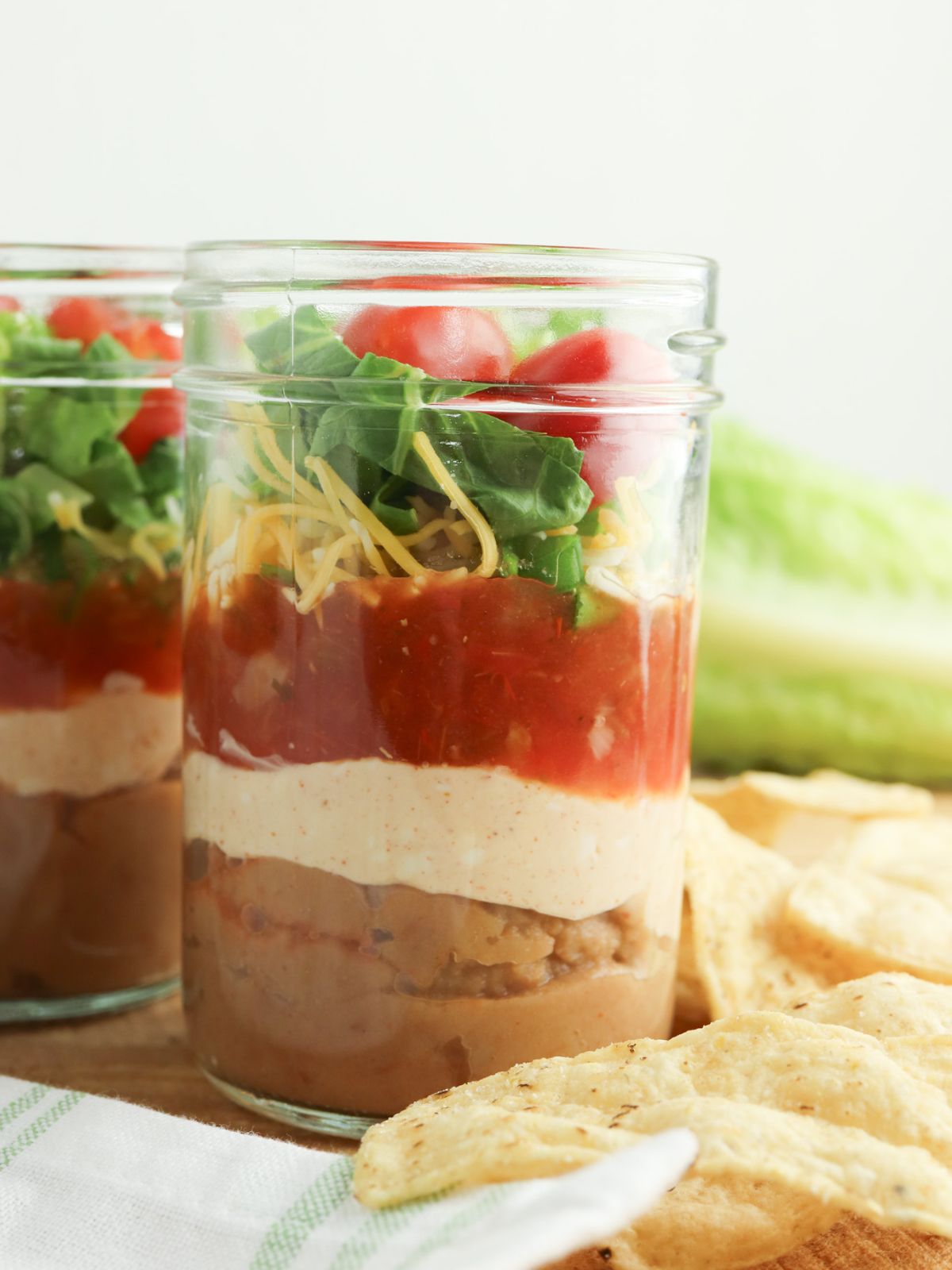 jar showing the layers of taco dip with tortilla chips on the side