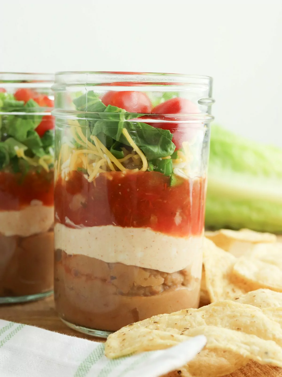 jar showing the layers of taco dip with tortilla chips on the side