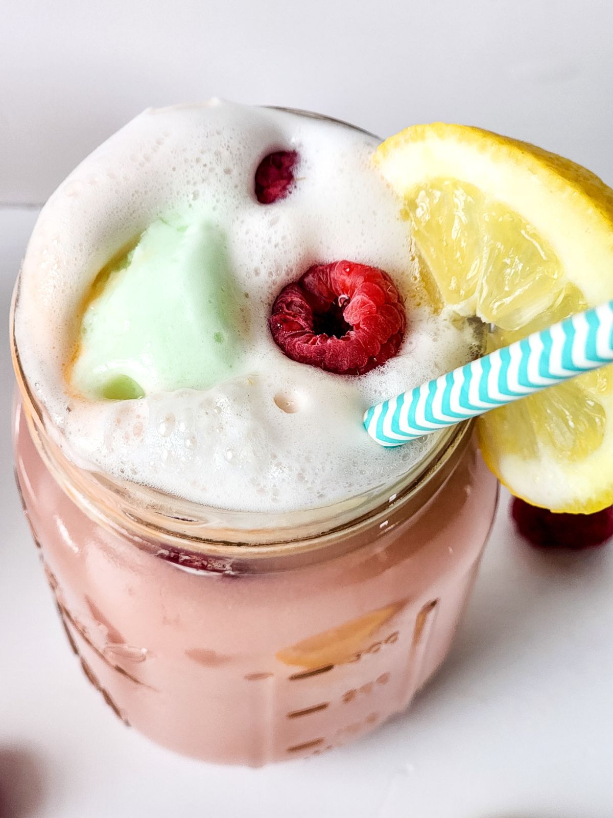 overhead view of mason jar filled with punch garnished with lemon, raspberries and teal straw