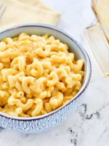 bowl of mac and cheese with casserole dish nearby.