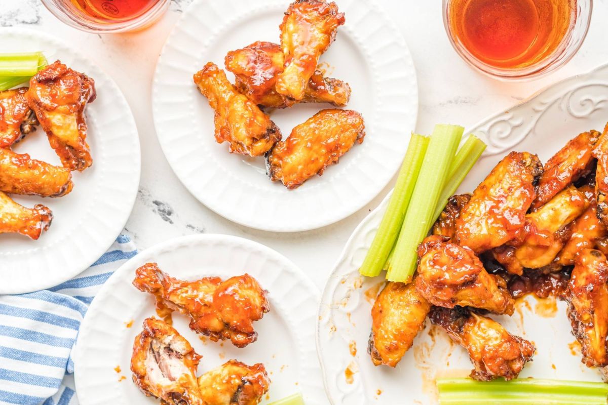 peach chicken wings on white plates with celery sticks.