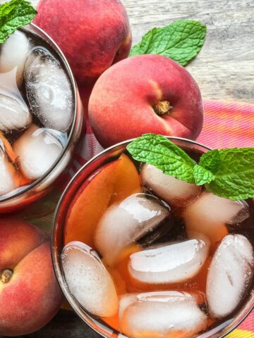2 glasses of peach iced tea with ice cubes and fresh peaches.