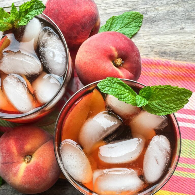 2 glasses of peach iced tea with ice cubes and fresh peaches.