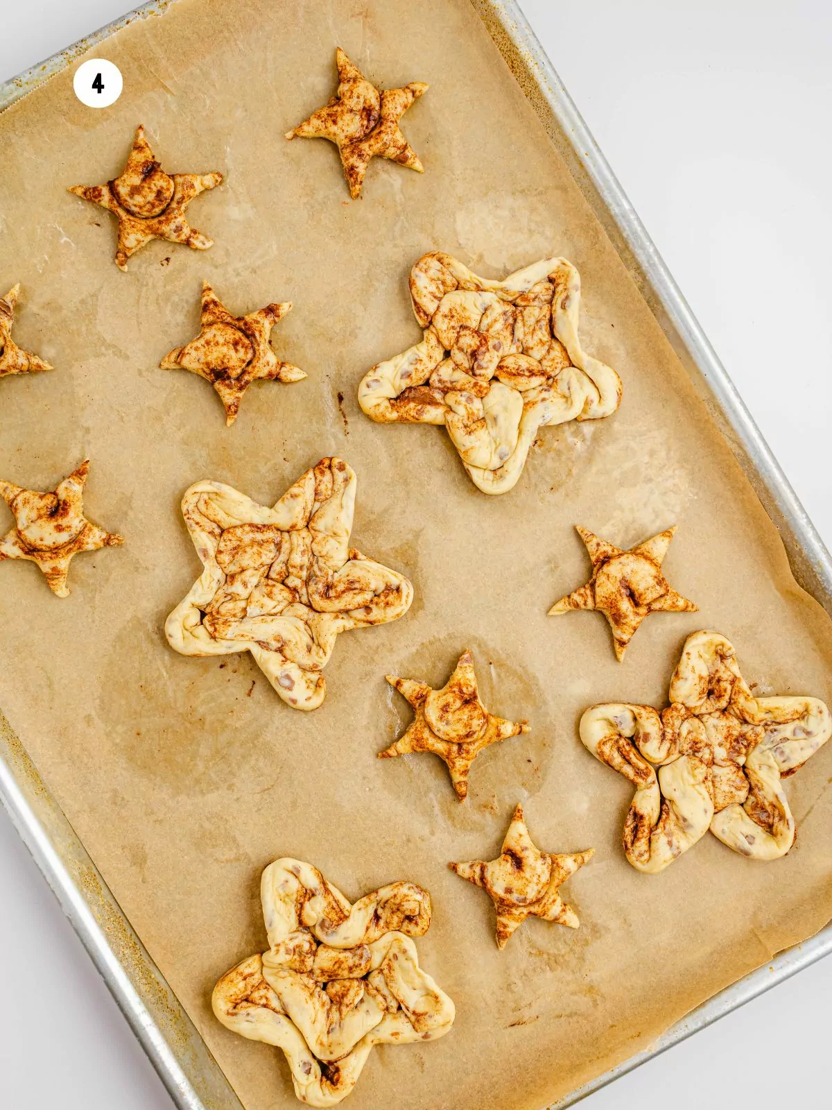 different sized star shaped cinnamon rolls on parchment lined baking sheet pan.