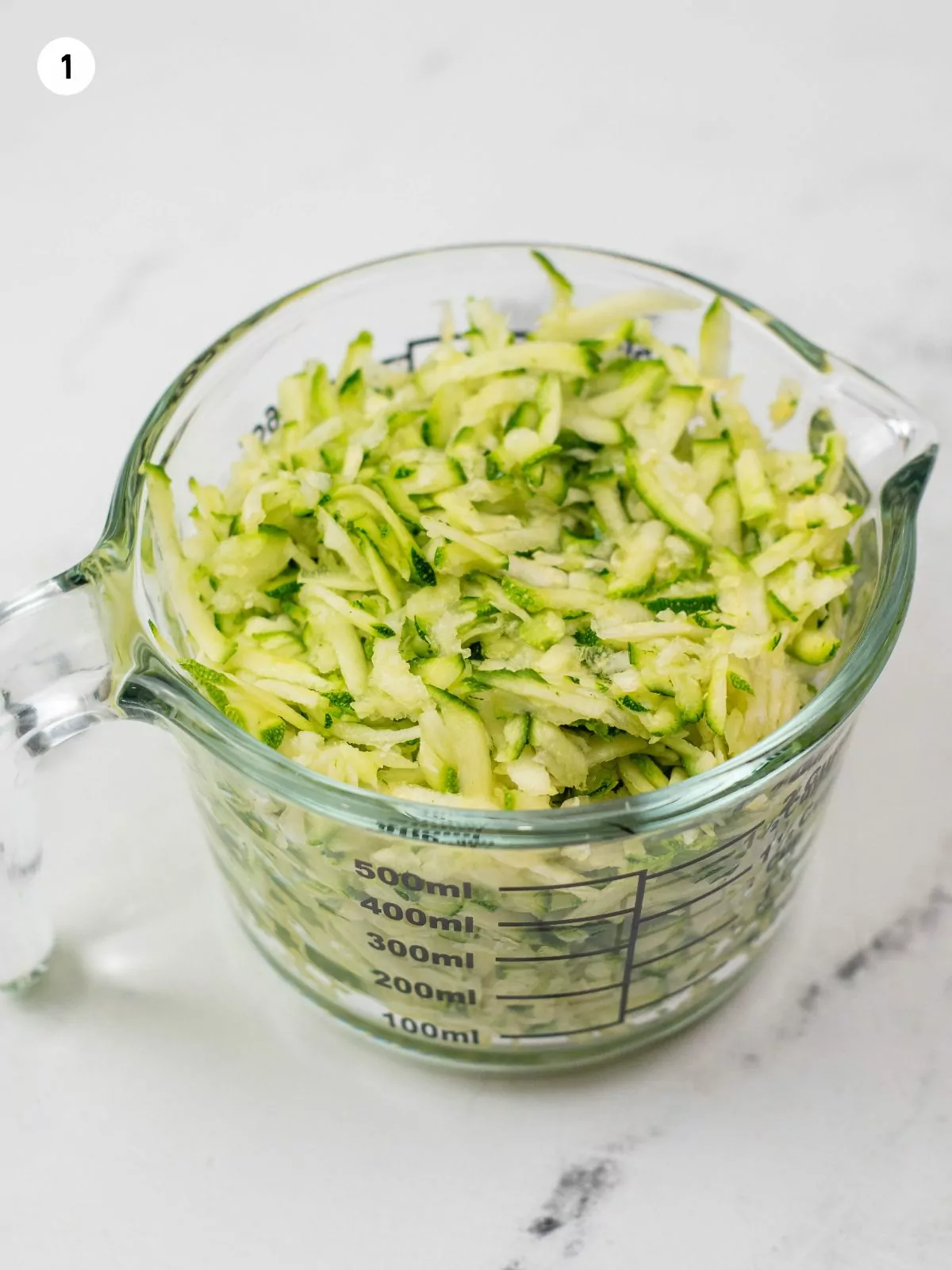 A measuring cup filled with shredded zucchini.