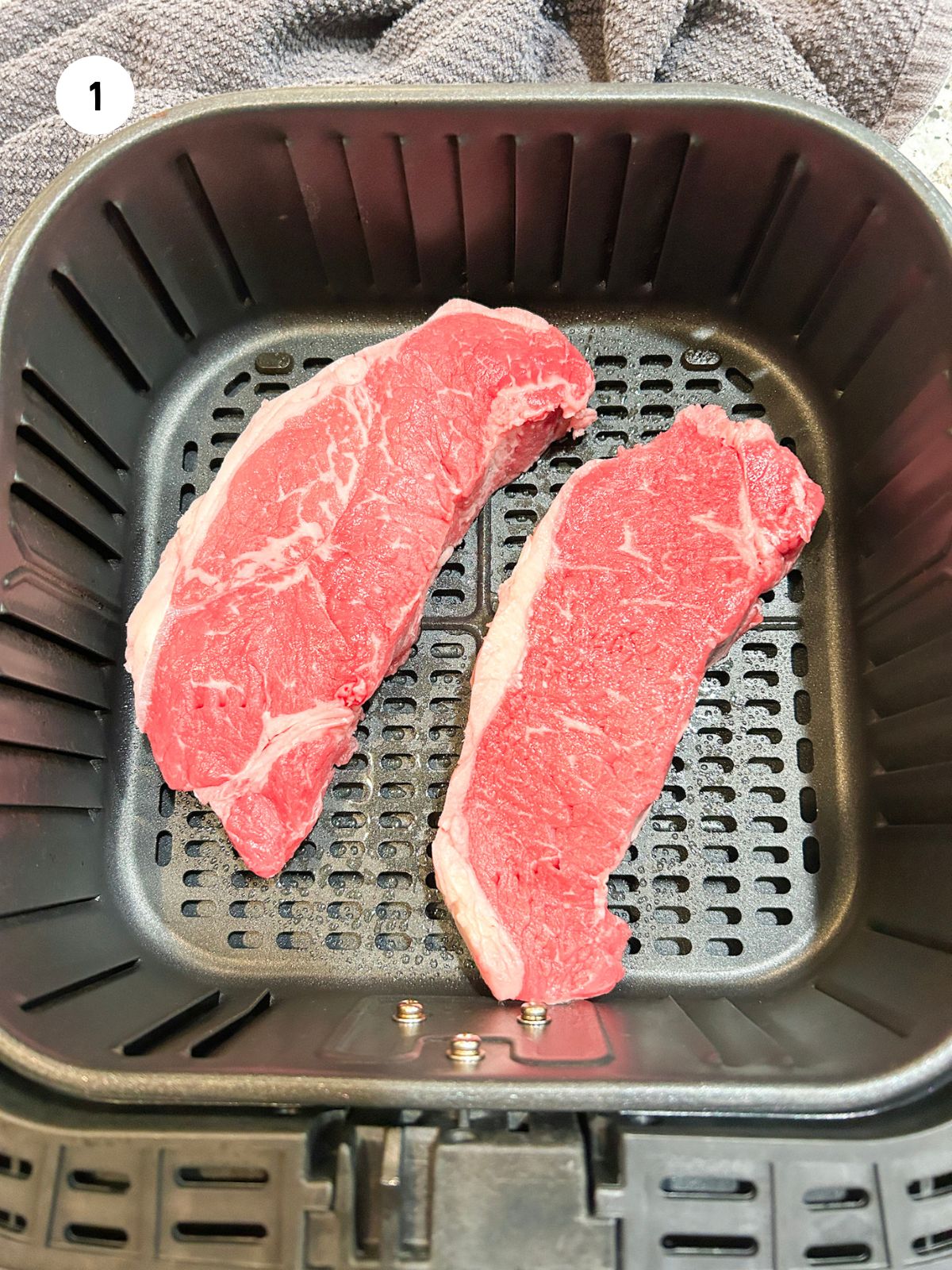 Two dry steaks placed in the air fryer basket.