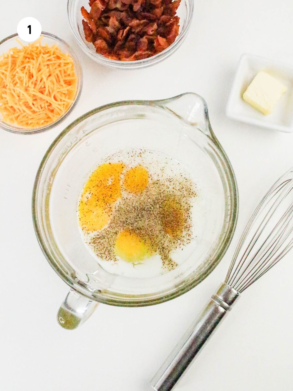 Eggs, milk, salt and pepper in a clear mixing bowl.