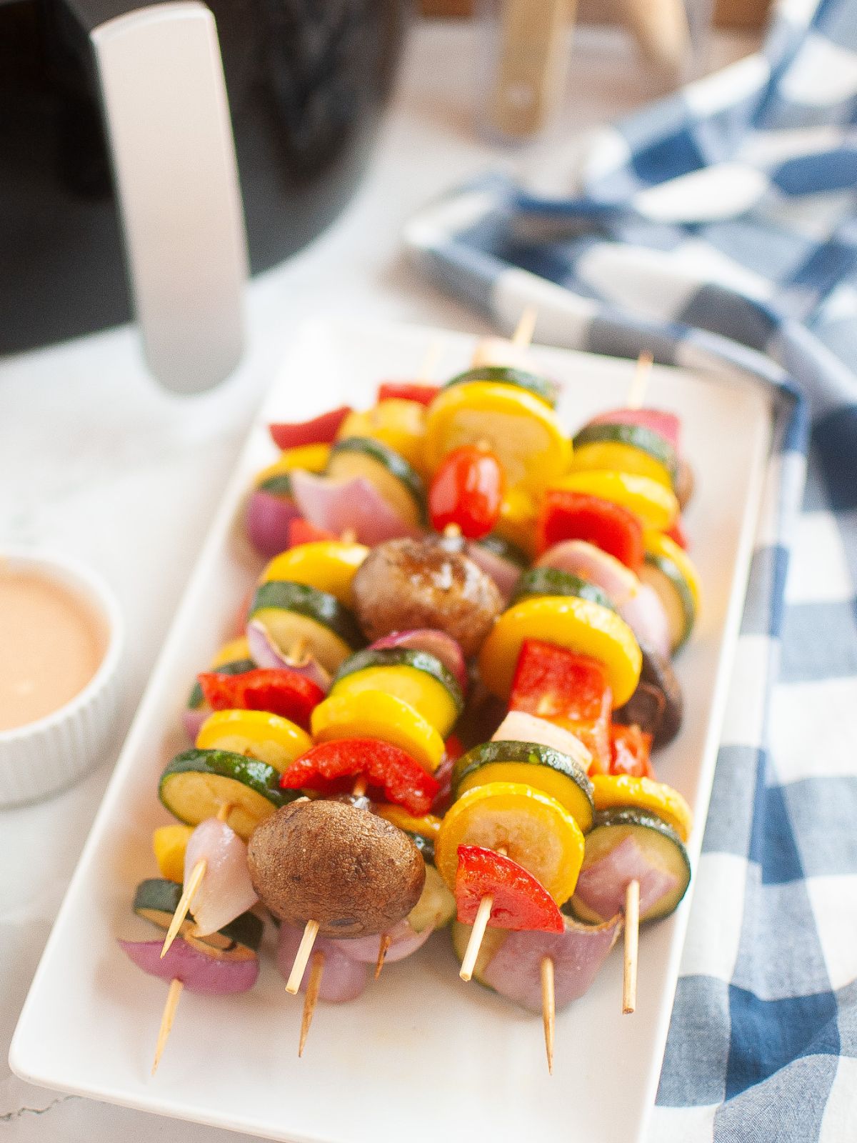 Pile of skewered air fried vegetables in front of an air fryer.