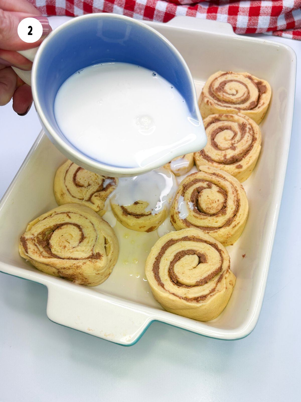 Pitcher pouring coffee creamer over the unbaked cinnamon rolls.