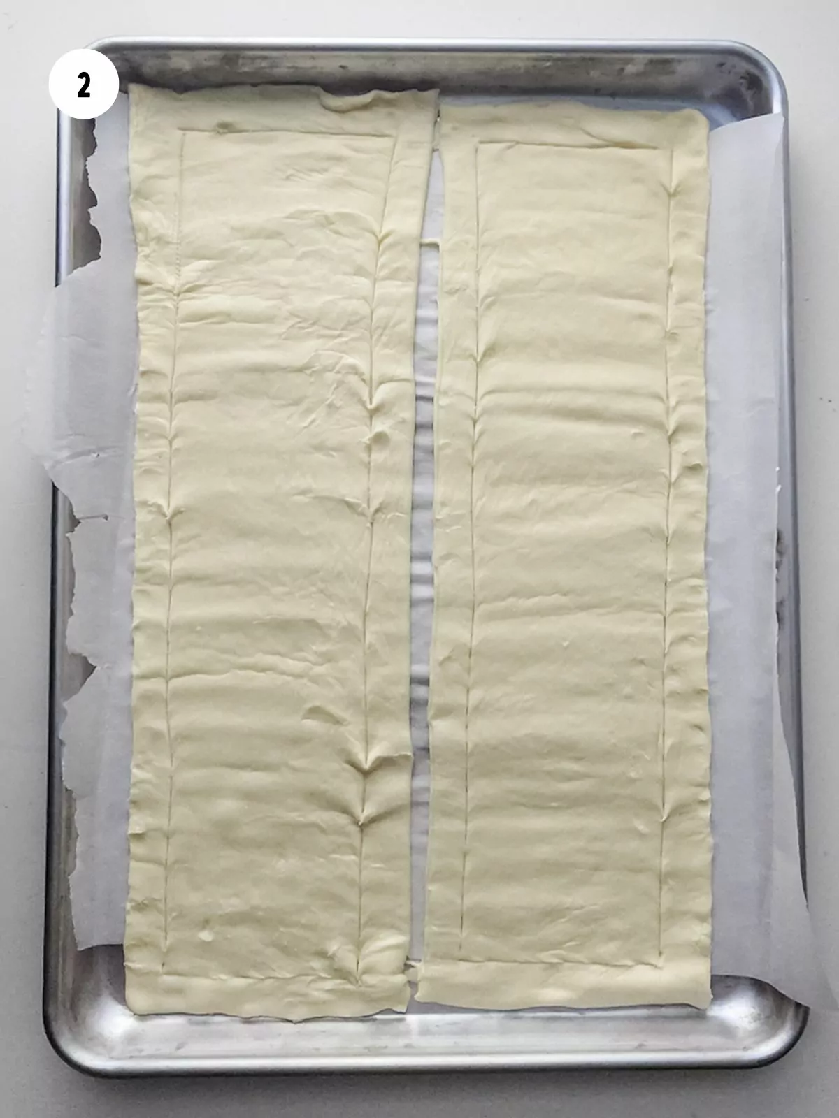 Two rectangles of scored puff pastry on a baking sheet.