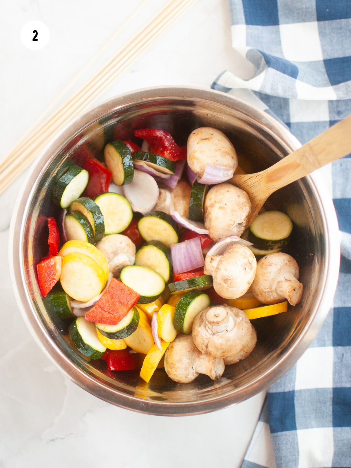 Large mixing bowl filled with mixed veggies tossed in oil and seasoning with a wooden spoon.