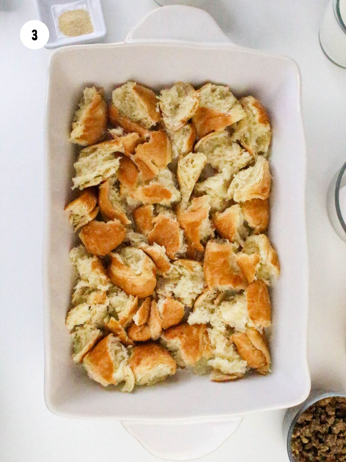 Torn croissants in the bottom of a white 9x13 casserole dish.