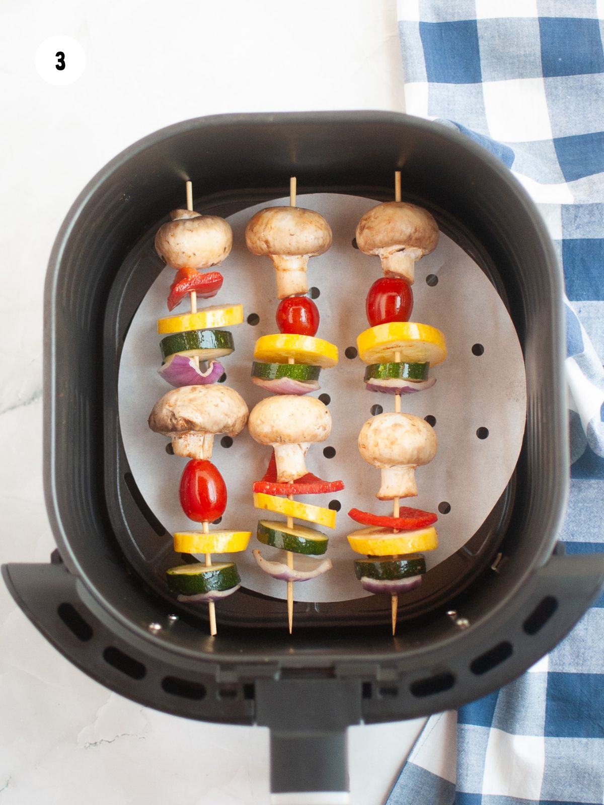 Three vegetable kabobs placed in an air fryer basket lined with parchment paper.