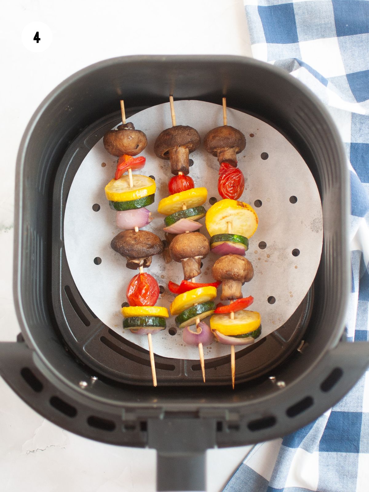 Three vegetable kabobs in an air fryer basket that have been cooked.