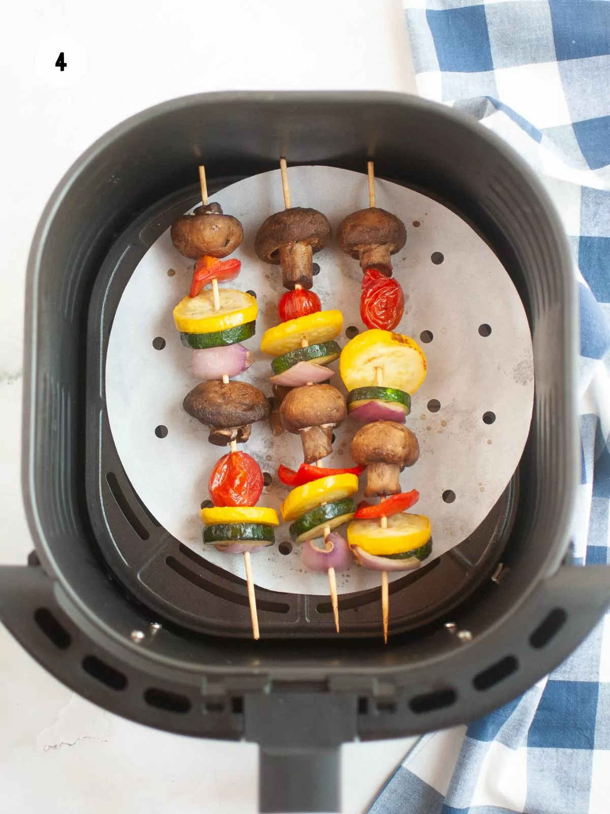 Three vegetable kabobs in an air fryer basket that have been cooked.