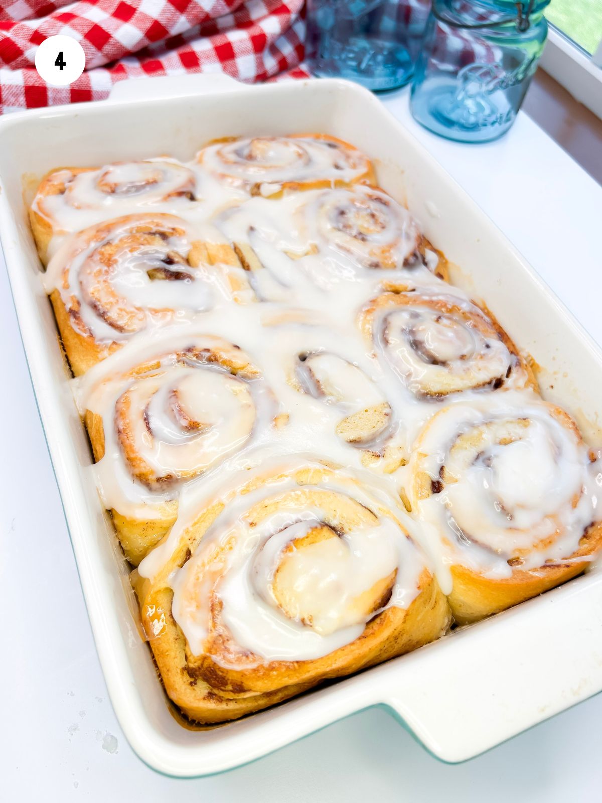 Baking dish filled with cinnamon rolls with icing on top.