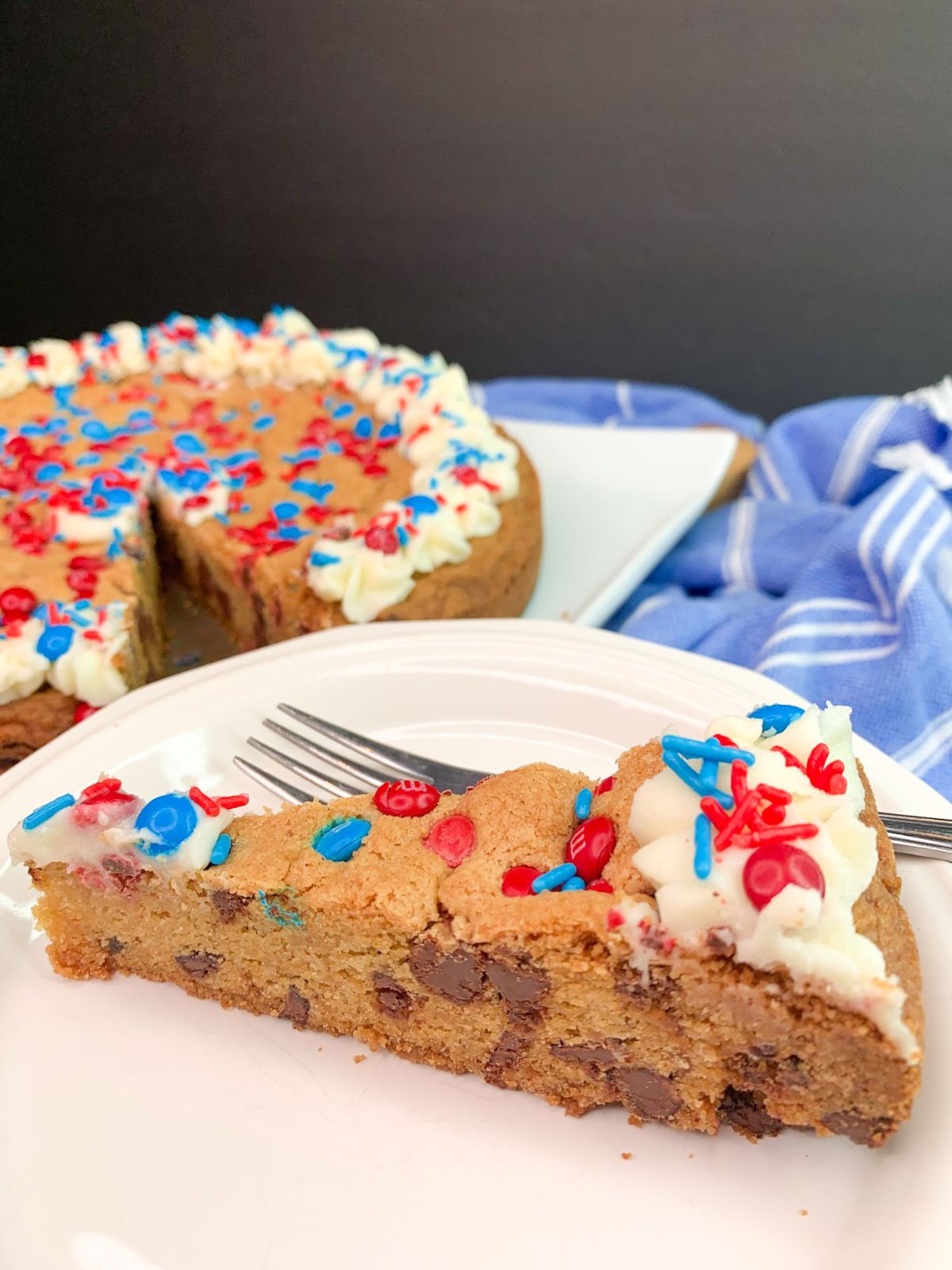 Slice of chocolate chip cookie cake decorated in red, white and blue with buttercream icing.