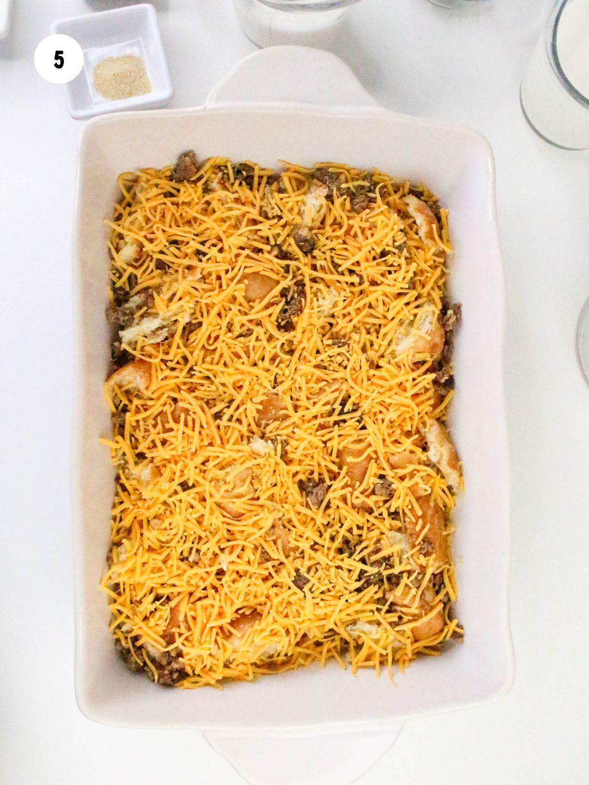 Shredded cheddar cheese on top of the sausage and croissants.