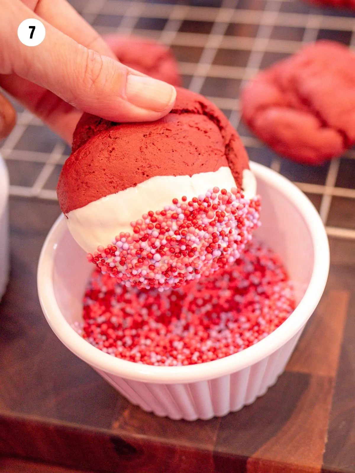 White chocolate dipped cookie being dipped into red and pink sprinkles.