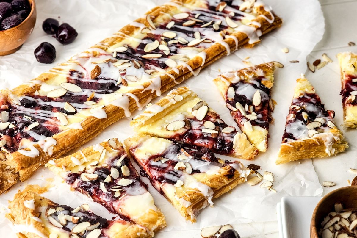 In the background is a rectangle Blueberry Danish and in the foreground another is cut into triangles.
