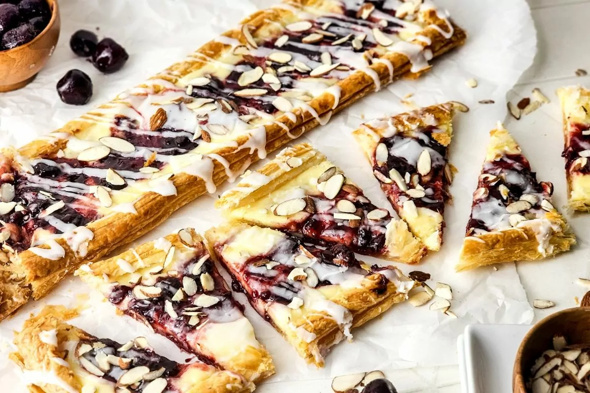 In the background is a rectangle Blueberry Danish and in the foreground another is cut into triangles.