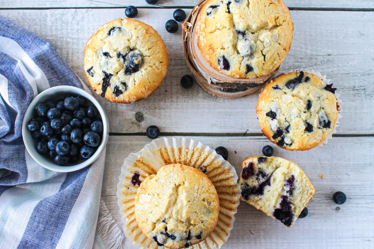 Overhead view of blueberry muffins with one cut in half to show the inside and a small bowl of fresh blueberries.