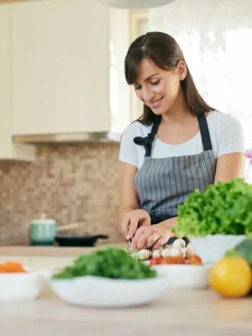 woman slice veggies for dinner surrounded by bowls of greens and fresh vegetables.
