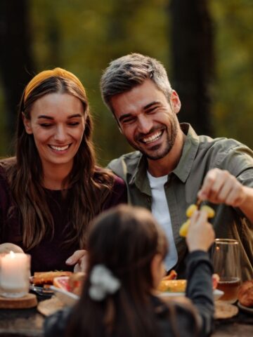 Couple enjoying their picnic with their family in the wood while eating grapes and laughing