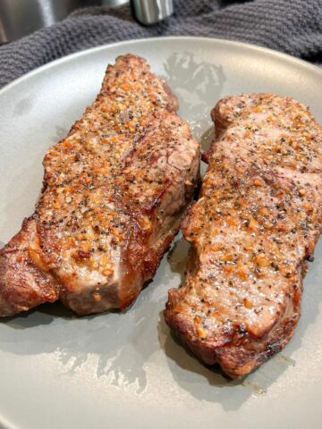 Two cooked NY Strip steaks served on a gray plate.