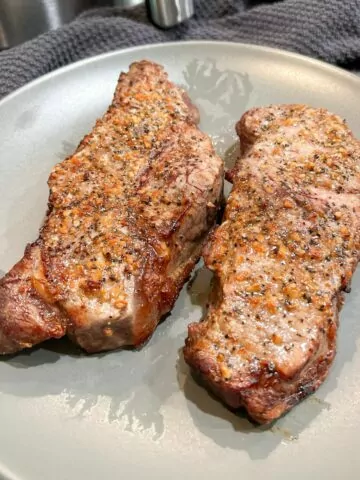 Two cooked NY Strip steaks served on a gray plate.