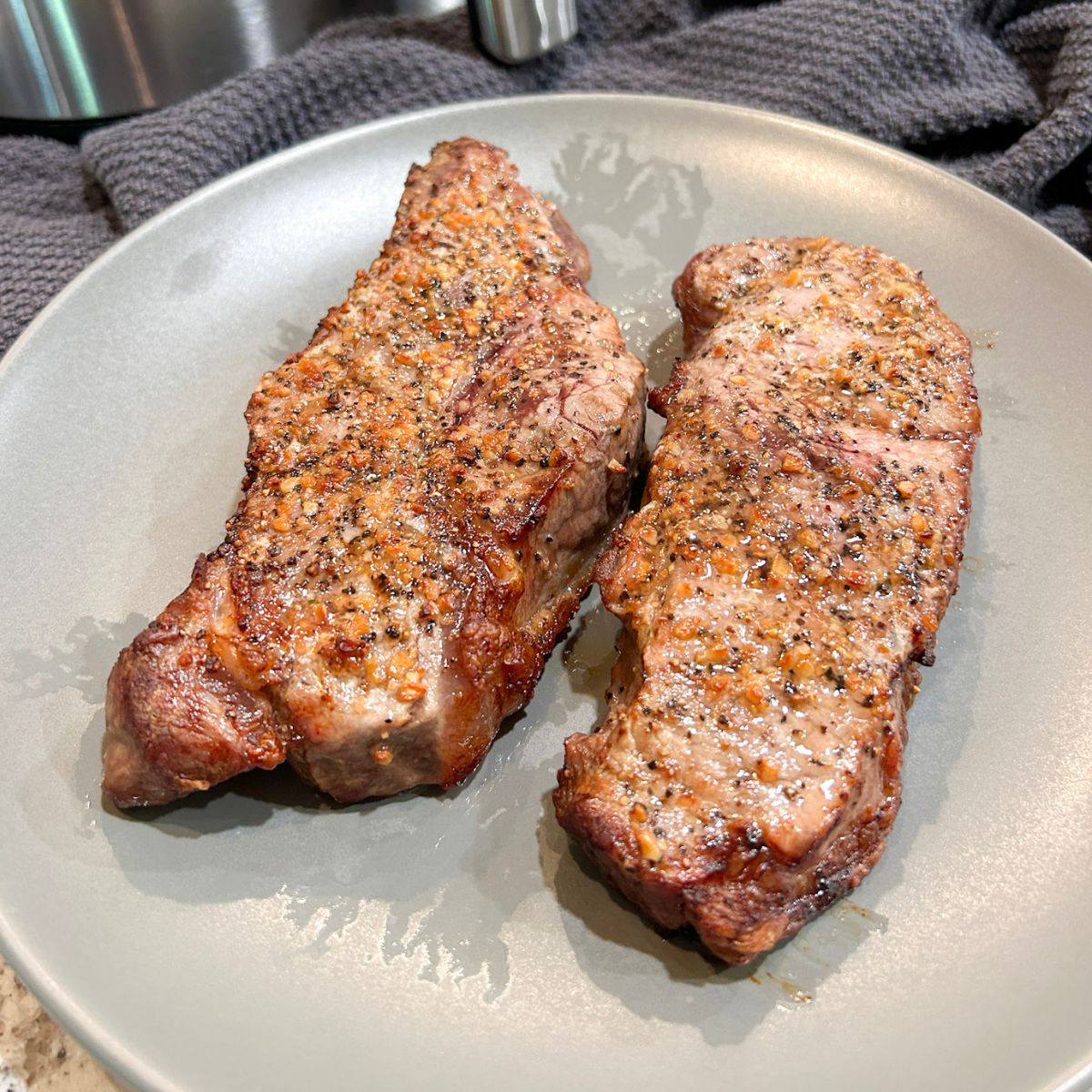 Two cooked NY Strip steaks served on a gray plate.