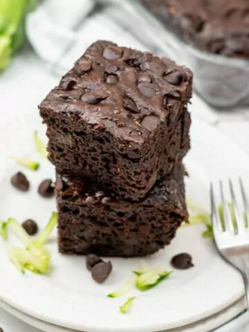 Two slices of chocolate zucchini cake stacked on a white plate.