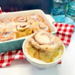 Big cinnamon roll served on a small pedestal with the baking dish in the background.
