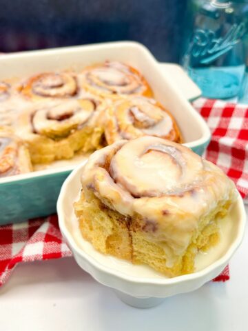 Big cinnamon roll served on a small pedestal with the baking dish in the background.