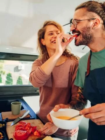 Happy young adult couple making breakfast together in cozy home kitchen in morning at home