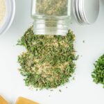 dried seasoning mix spilling out of a glass bottle on white surface.