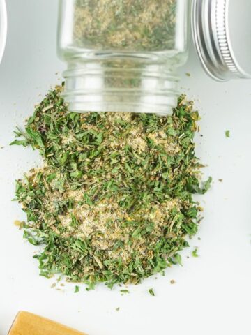 dried seasoning mix spilling out of a glass bottle on white surface.