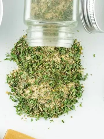 dried seasoning mix spilling out of a glass bottle on white surface.