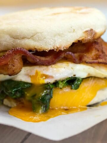 breakfast sandwich with bacon, egg, spinach, cheese on English muffin.