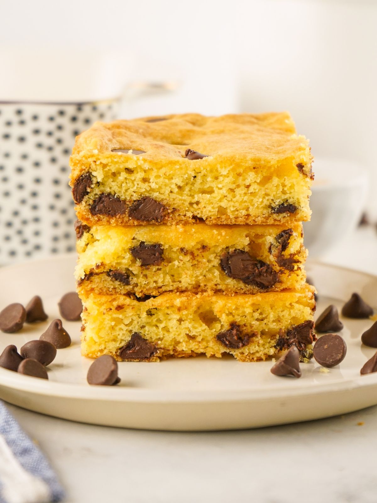 chocolate chip bars using cake mix stacked on plate with extra chocolate chips scattered around.