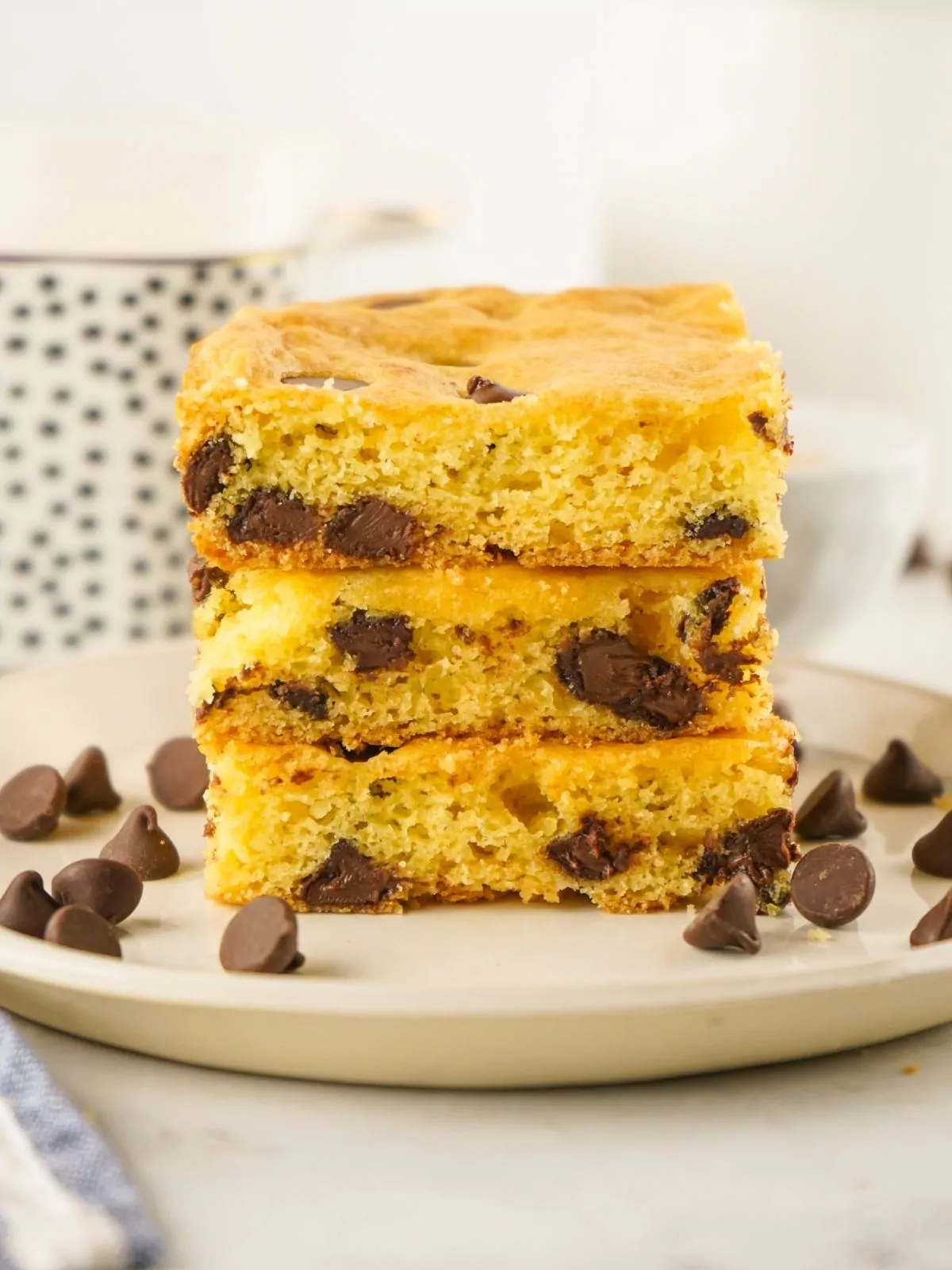 chocolate chip bars using cake mix stacked on plate with extra chocolate chips scattered around.
