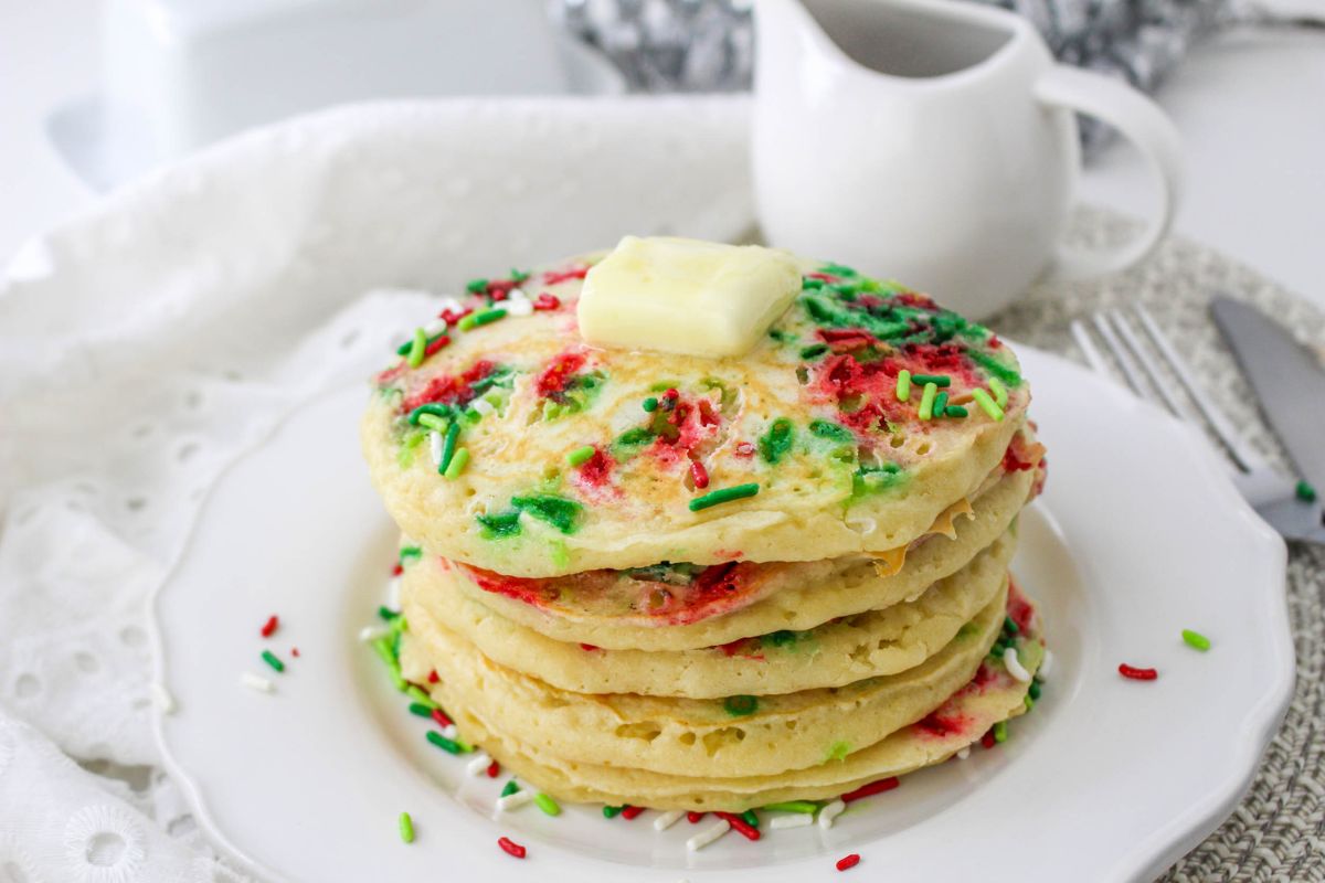 stack of pancakes with Christmas sprinkles and a pat of butter on a white plate.