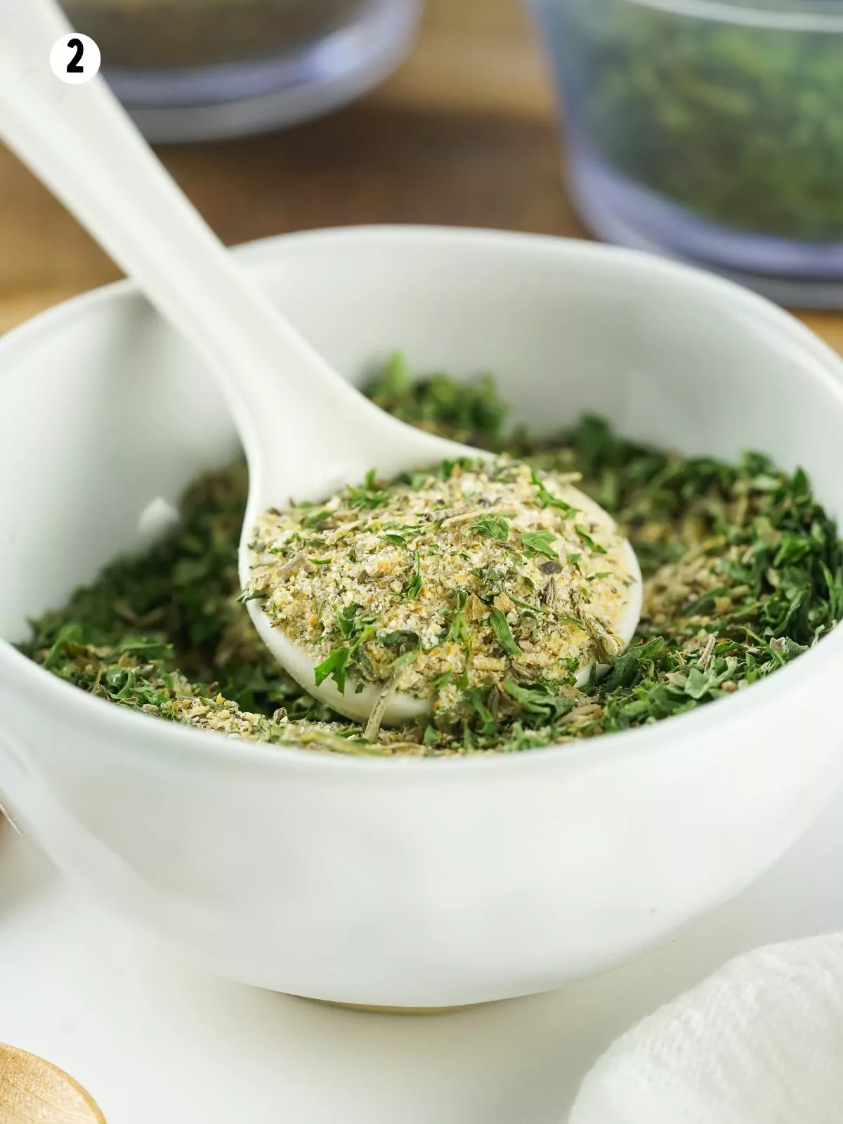 small white spoon scooping out homemade dried herbs for seasoning mix.